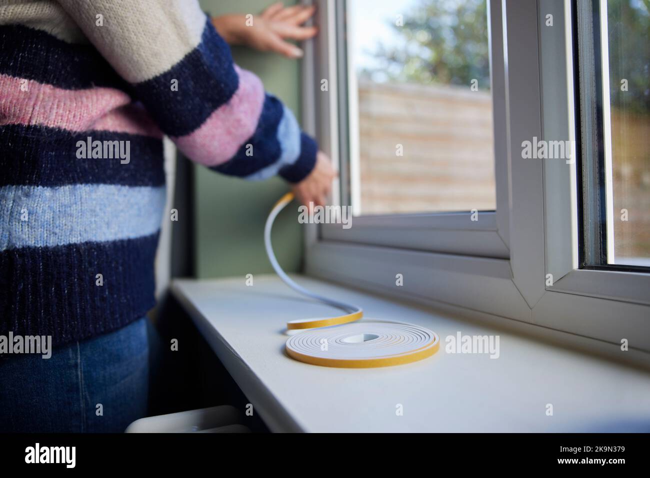 Mujer salvando enegy aislamiento Home Poniendo cinta de exclusión de draught en la ventana Foto de stock
