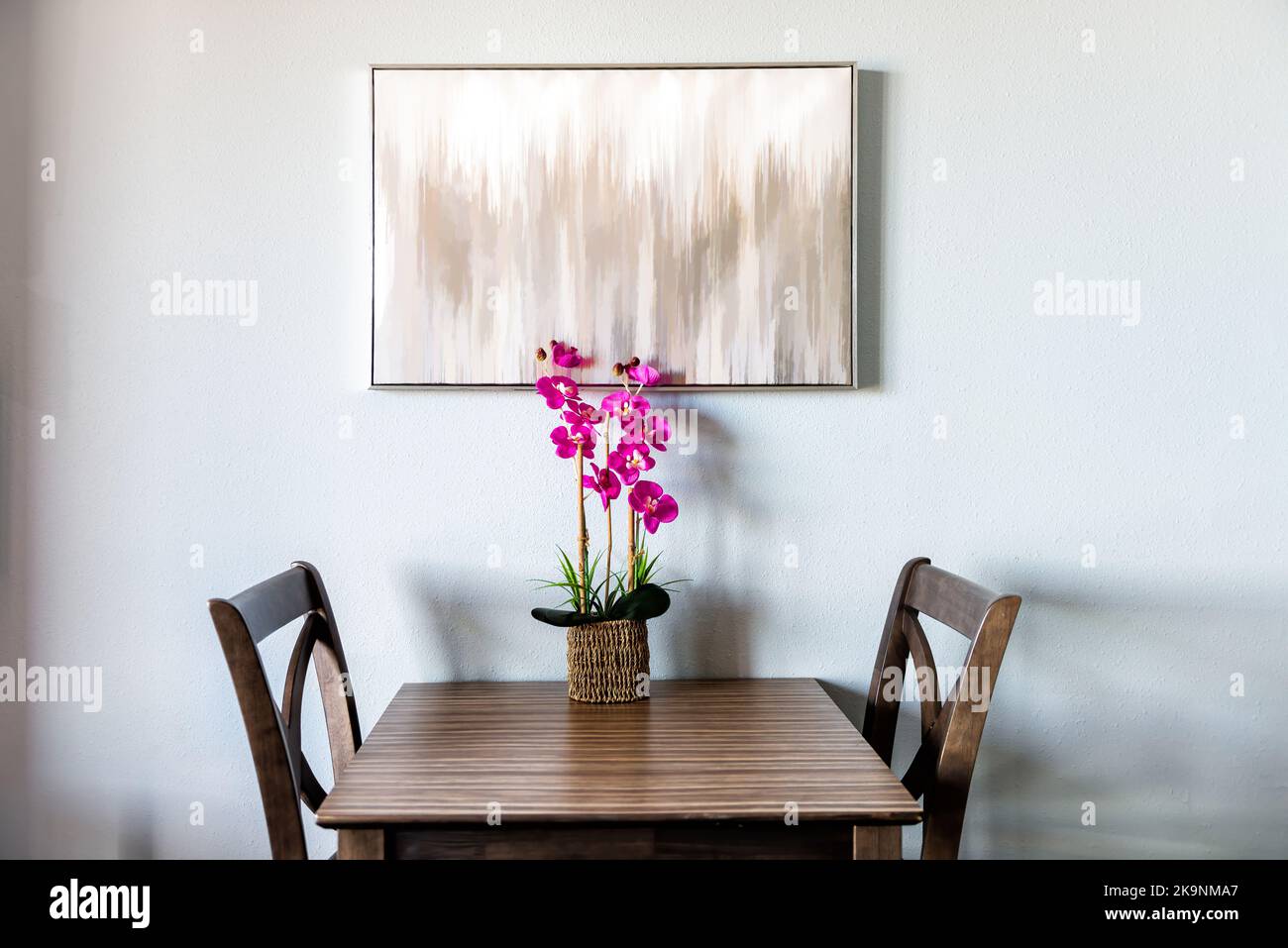 Minimalismo minimalista vista sobre dos sillas por mesa con pintura moderna y orquídeas flores en macetas artificiales en jarrón de olla por la pared blanca de la habitación del apartamento Foto de stock