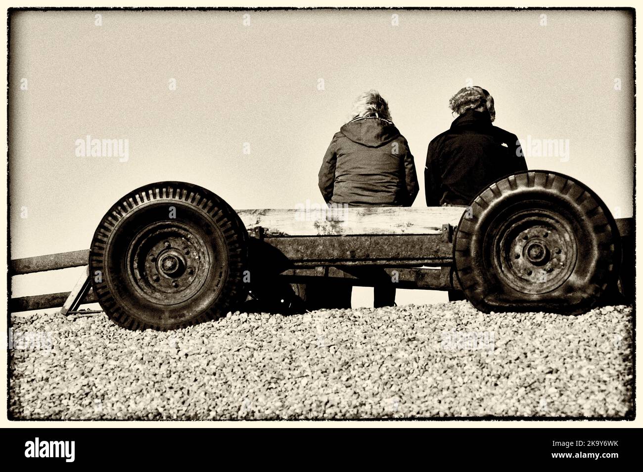 dos personas sentadas en un viejo remolque con neumático desinflado en la playa de guijarros weybourne norfolk england Foto de stock