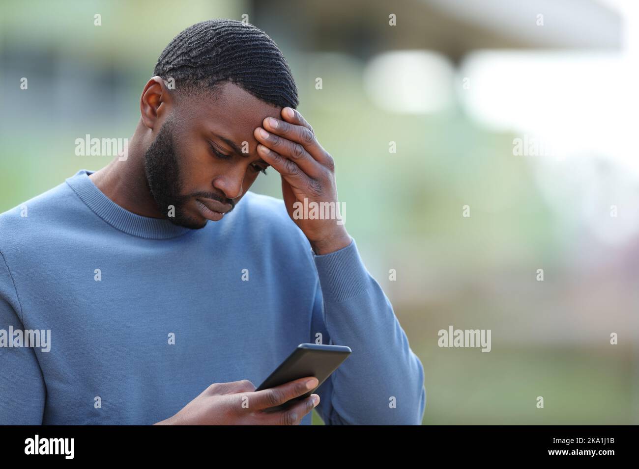 Hombre negro preocupado leyendo malas noticias en el teléfono inteligente en la calle Foto de stock