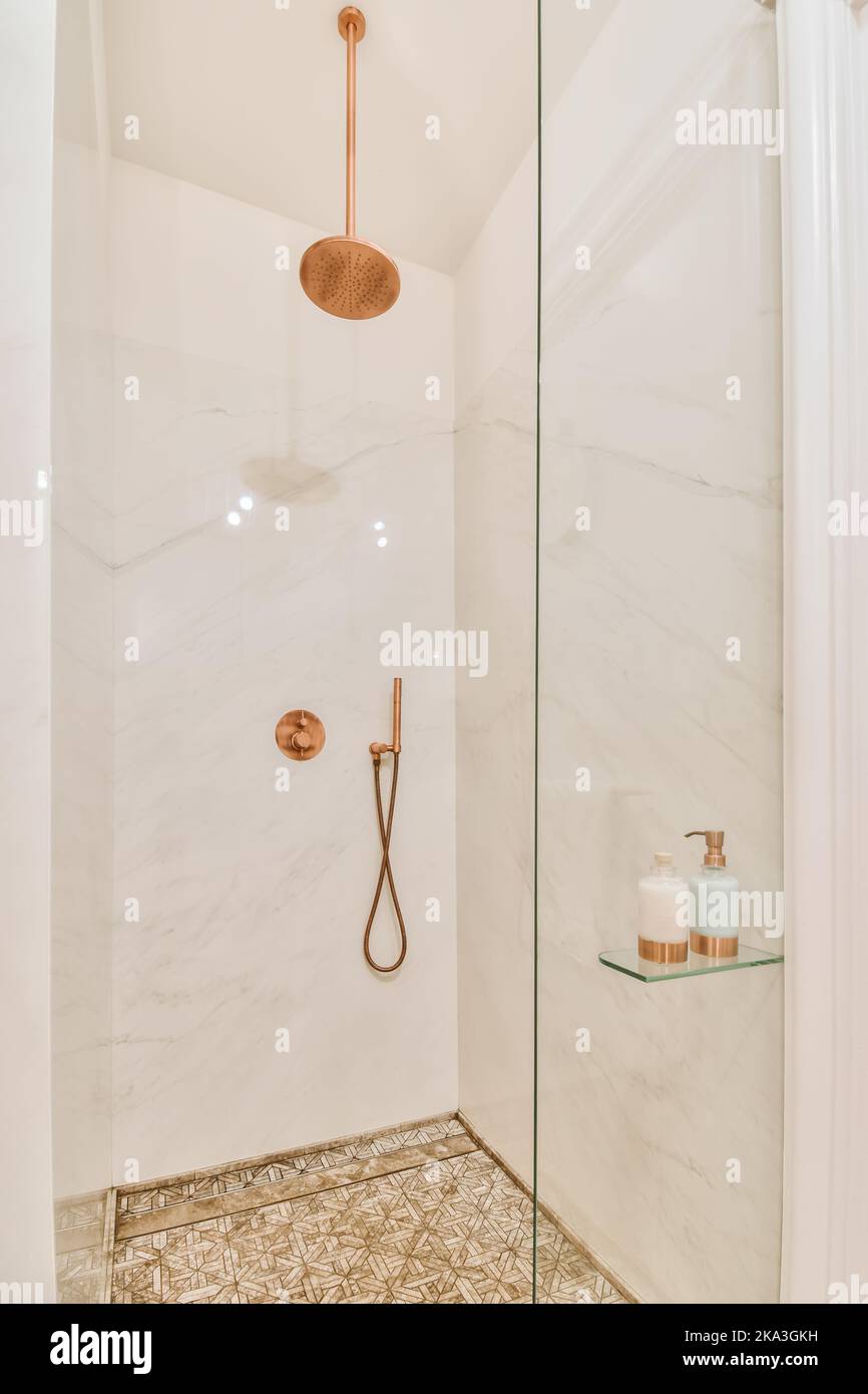 Ducha moderna con grifos de cobre en un baño moderno y luminoso con paredes de mármol blanco Foto de stock