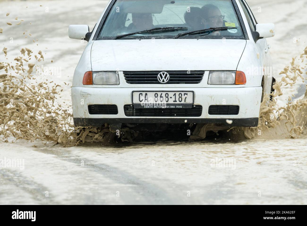 El automóvil sedán blanco conduce a través de una carretera cubierta de espuma marina durante una tormenta de invierno en Ciudad del Cabo, Sudáfrica Concepto de seguridad vial Foto de stock