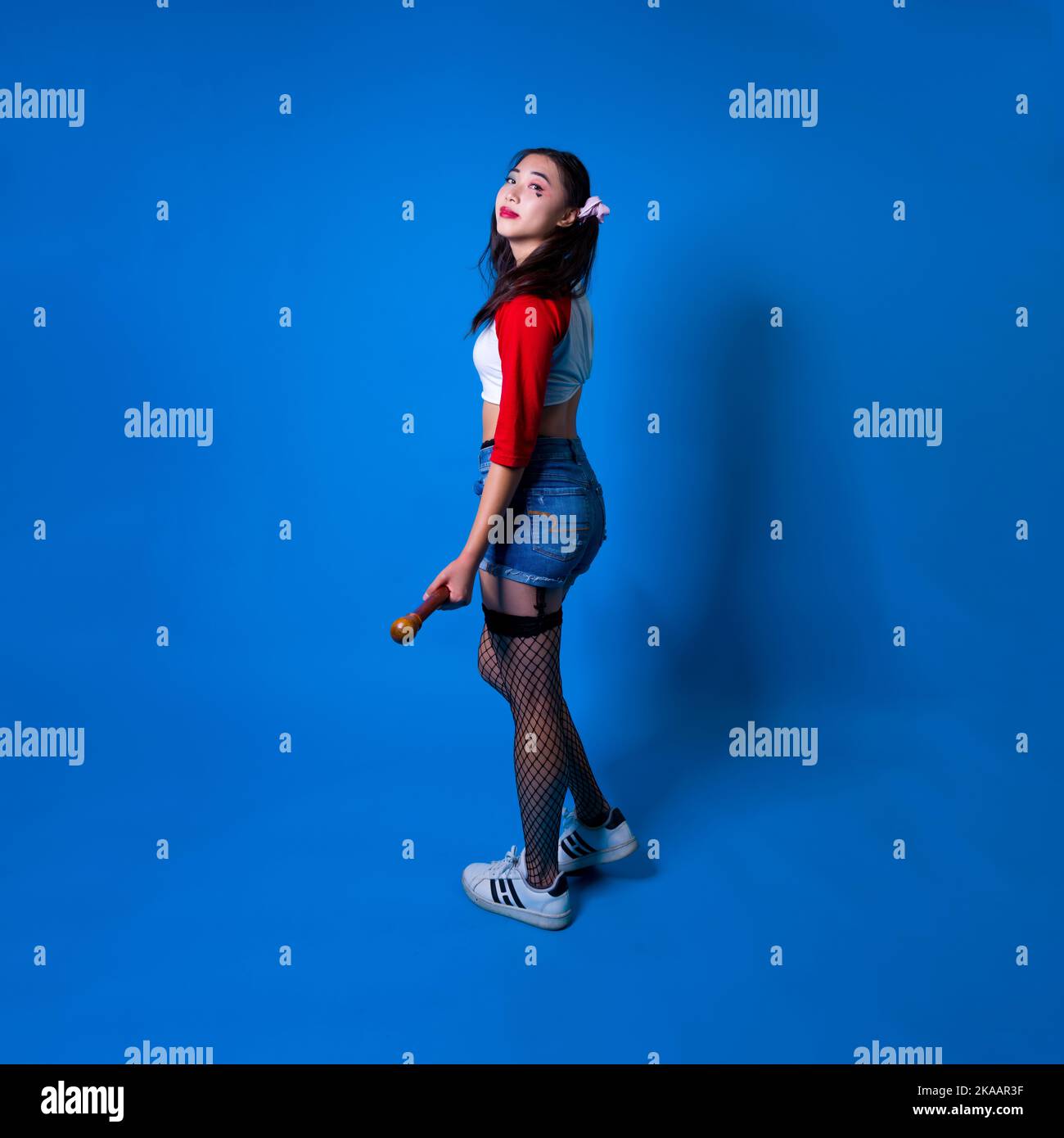 Mujer joven en traje Harlequin de pie frente a fondo azul con espacio de copia Foto de stock