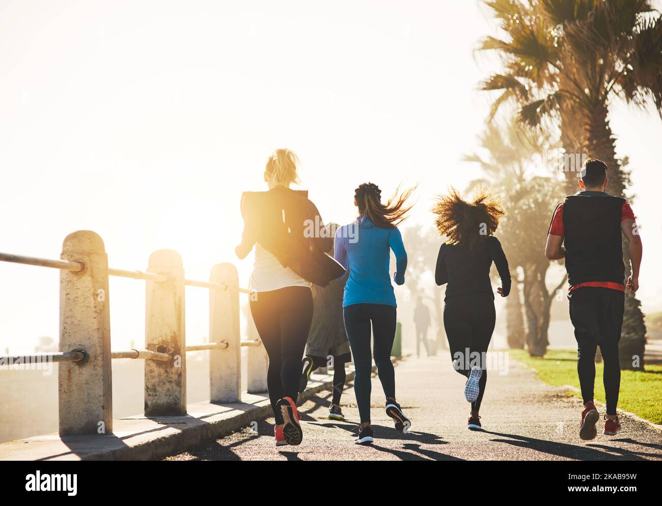 Porque su no diversión que trabaja hacia fuera por se. Imagen trasera de un grupo de fitness corriendo por el paseo marítimo. Foto de stock