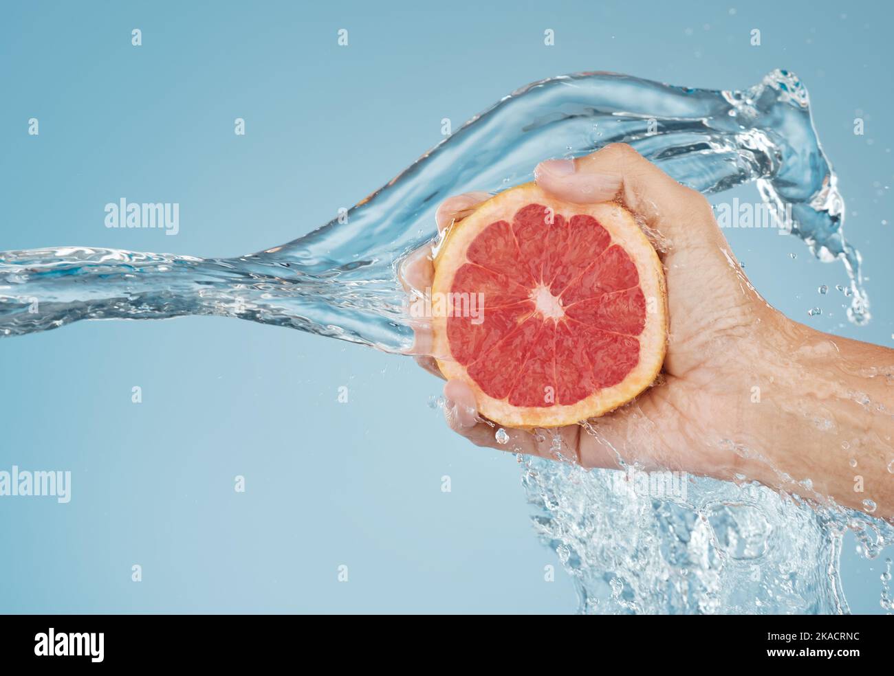 Pomelo, agua y mano con un alimento de verano para la salud, la nutrición y la dieta contra un fondo azul del estudio de la mockup. Splash, tropical y persona Foto de stock