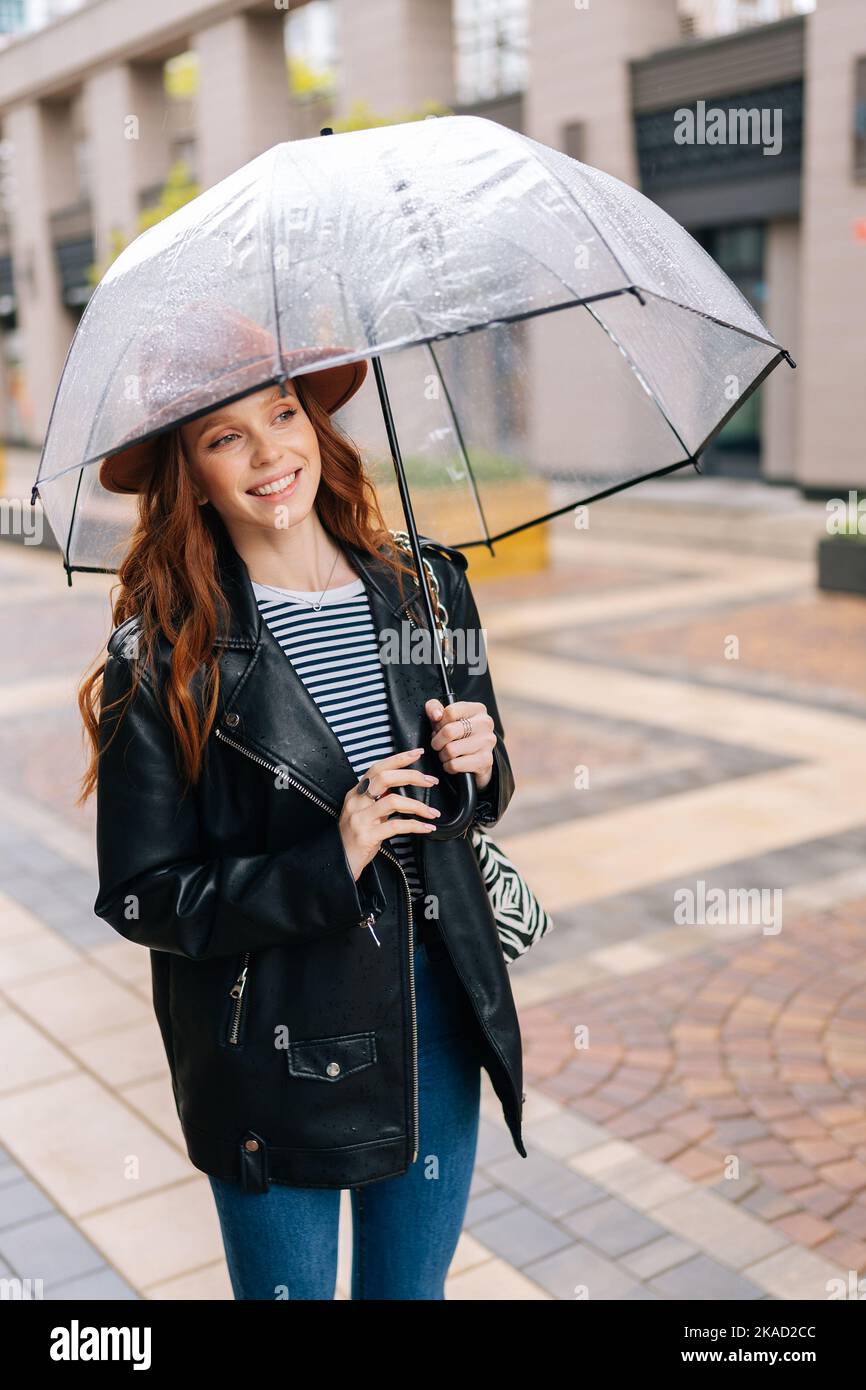Chica joven con chubasquero amarillo con paraguas transparente en la  ciudad. Joven hermosa mujer con traje de lluvia y gafas mientras camina en  la calle. Con Fotografía de stock - Alamy
