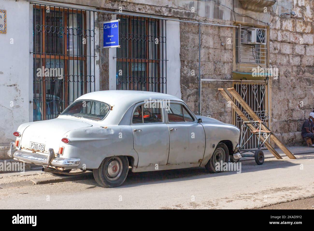 Un coche gris vintage está aparcado junto a un carro rústico. Hay un contraste arquitectónico entre un edificio viejo y otro en buen estado. Foto de stock