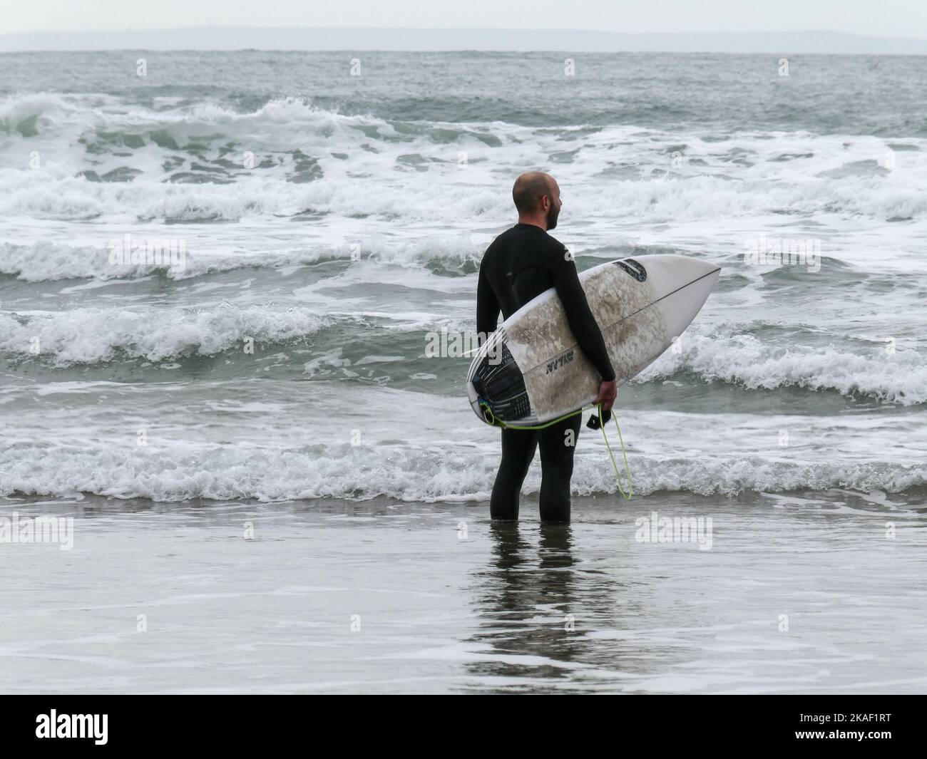 Un surfista con traje de neopreno tiene una tabla corta mientras las olas rompen en la playa de Putsborough en Devon, Inglaterra Foto de stock