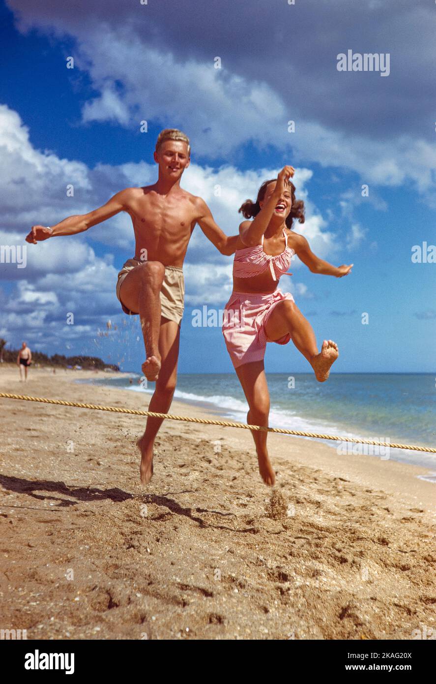 Hombre adulto joven y mujer joven saltando sobre la cuerda en Sandy Beach, Florida, EE.UU., Toni Frissell Collection Foto de stock