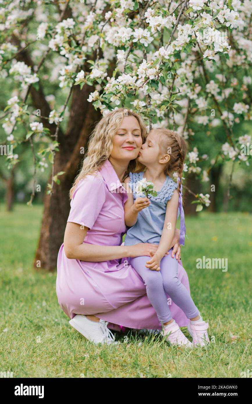Hija besa mamá en la mejilla en el parque de primavera Foto de stock