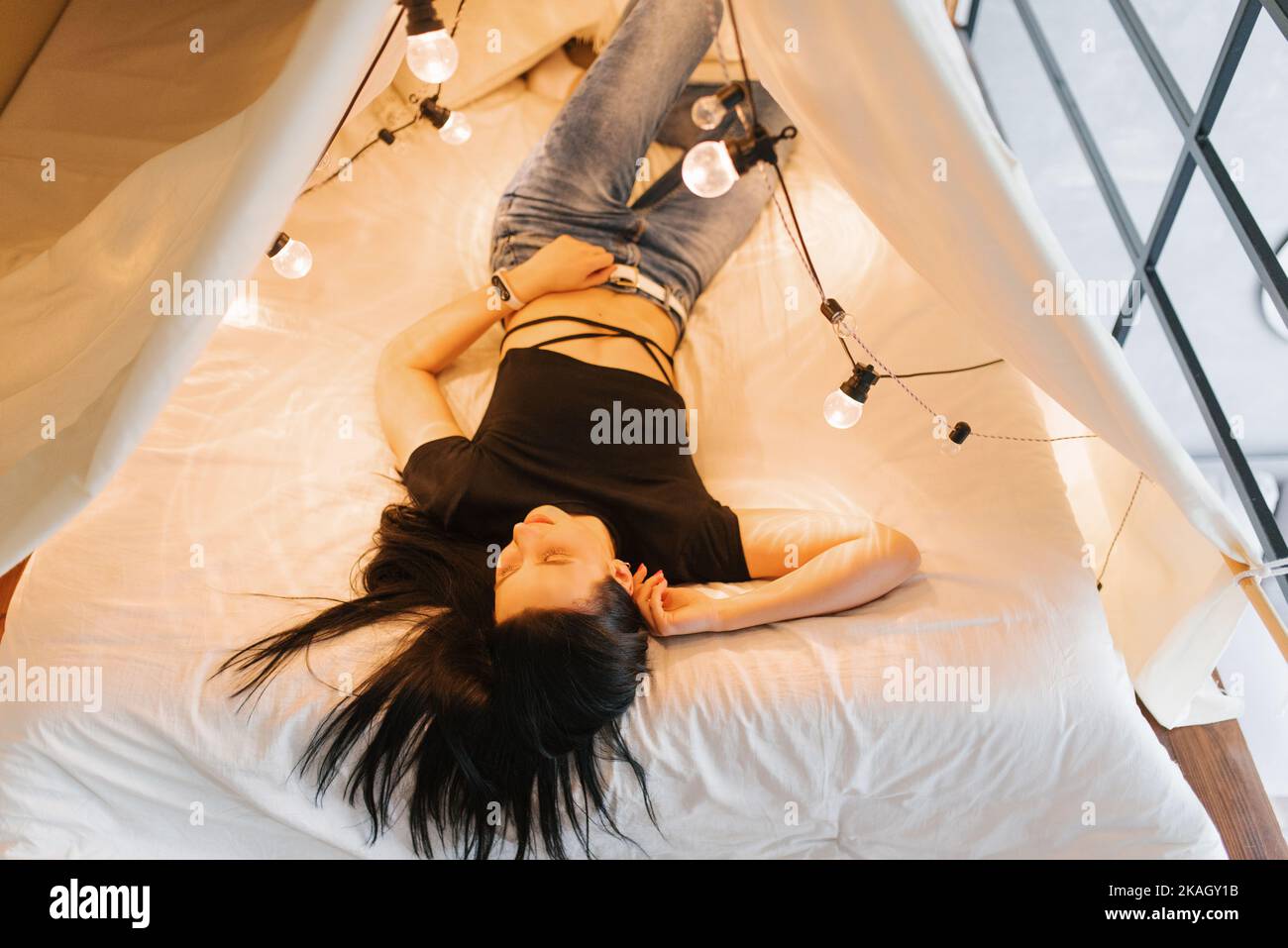 Una mujer joven está acostada en una cama con dosel con bombillas brillantes Foto de stock