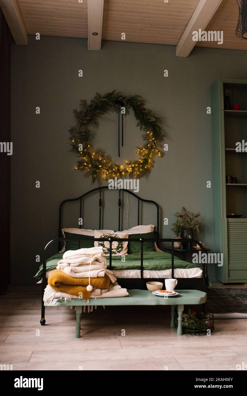 Dormitorio decorado para las vacaciones de Navidad con una corona en la pared y decoración en verde Foto de stock