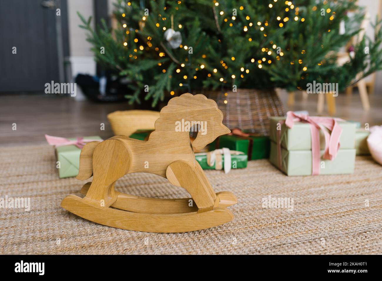 Silla de ruedas de juguete a caballo de madera sobre el fondo de las luces del árbol de Navidad y regalos con espacio para copias Foto de stock