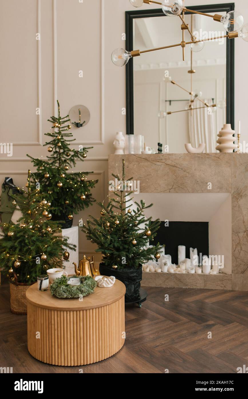 En la sala de estar hay varios árboles de Navidad elegantes junto a la chimenea de mármol Foto de stock