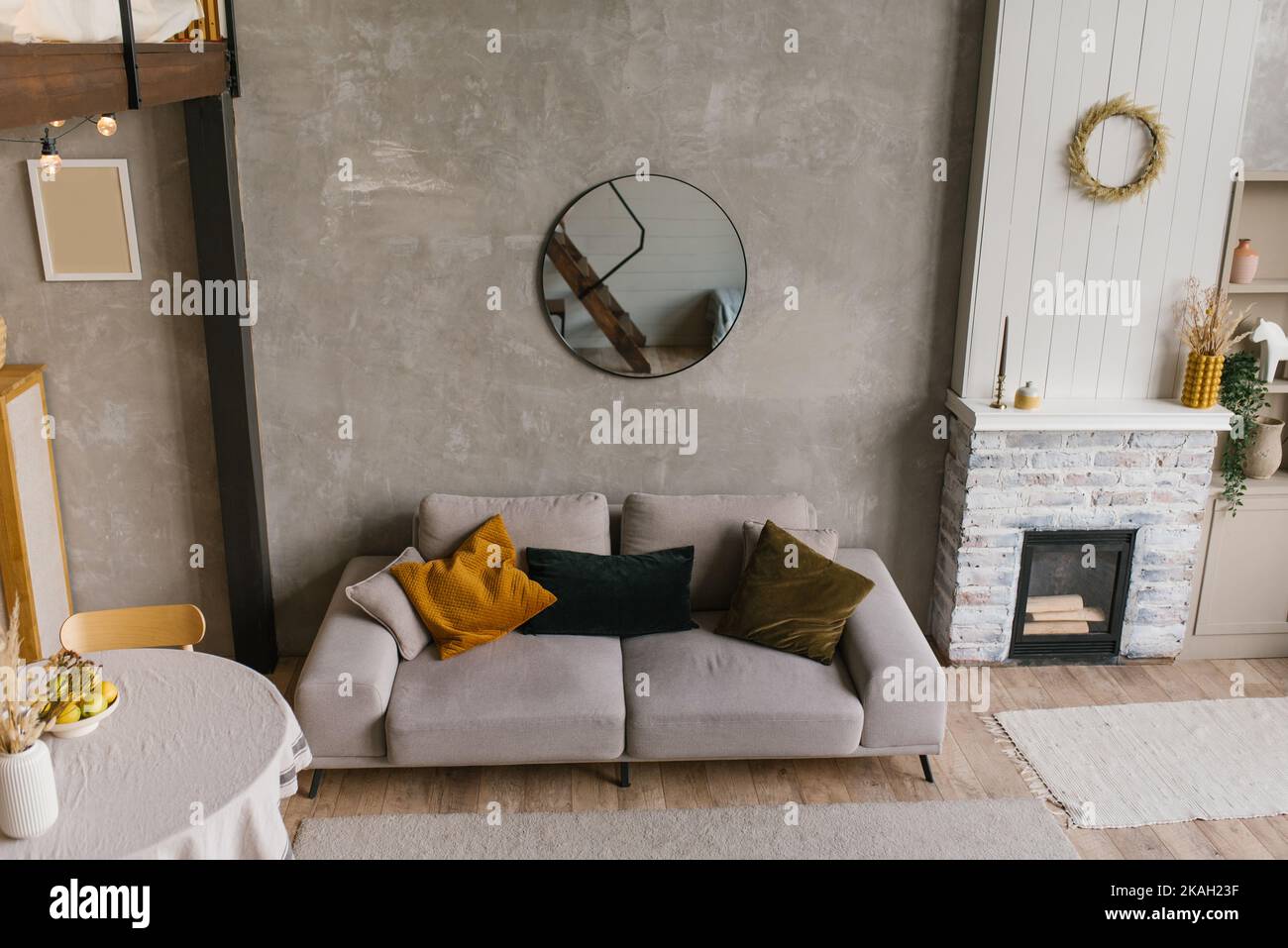 Acogedor interior de estilo escandinavo de una sala de estar con un sofá gris con almohadas, una mesa de comedor redonda y una chimenea en una casa de campo Foto de stock