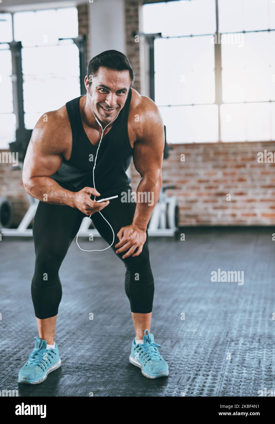 Hombre musculoso atlético en auriculares inalámbricos escuchando música  durante el entrenamiento en el gimnasio