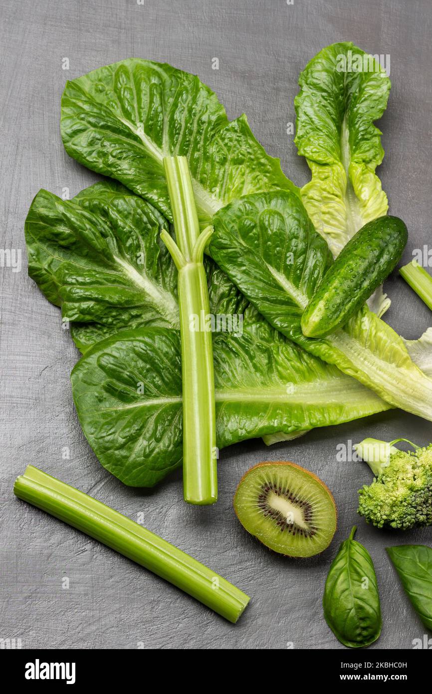 Juego de verduras verdes. Lechuga, tallos de apio, medio kiwi y pepino. Colocación plana. Fondo gris. Foto de stock