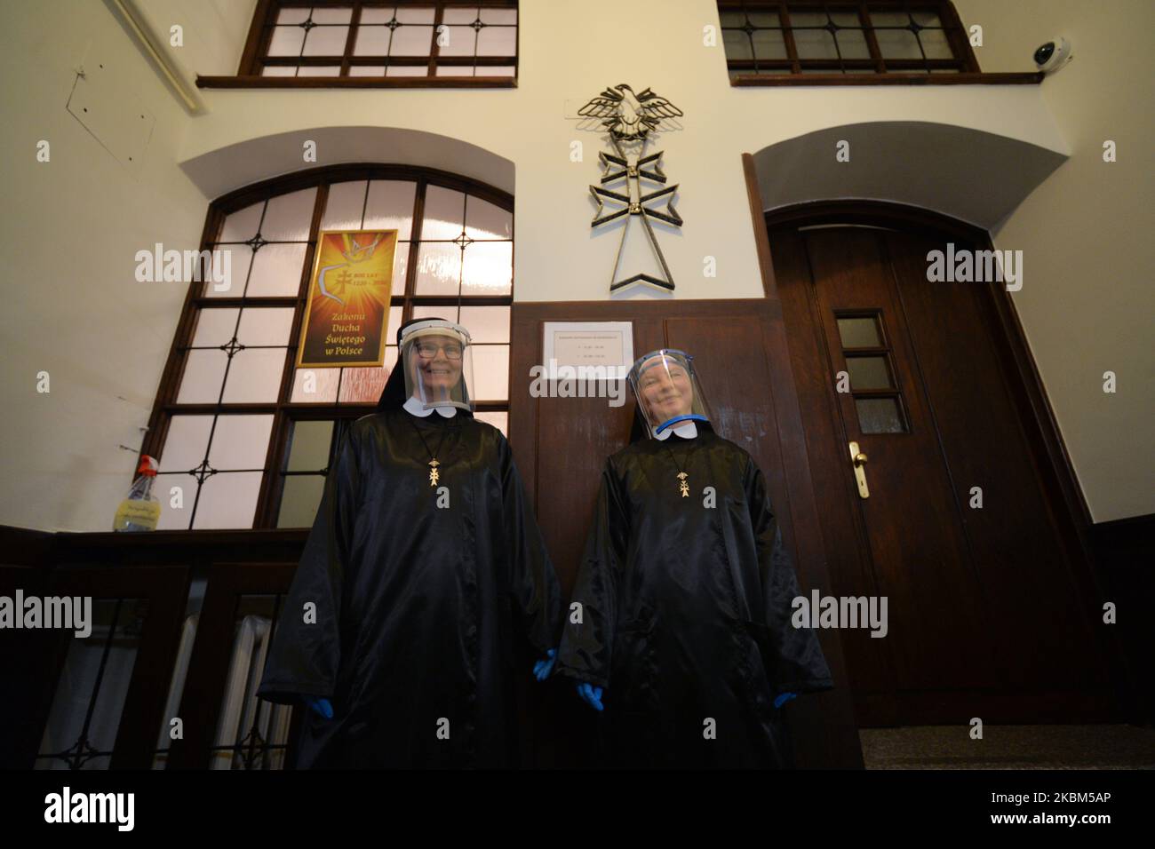 Monjas de la orden religiosa de las Hermanas del Canon del Espíritu Santo, usando equipo de protección pesonal dentro de la entrada de su convento, antes de distribuir comida a los pobres. Las hermanas se solidarizan con toda persona que necesita su presencia y oraciones, y responden a las necesidades de las crisis del coronavirus ayudando a los sin hogar. Cada día las monjas abren la ventana de su convento llamada 'Gwidon's Window' (nombre del fundador de la orden) en el centro de Cracovia, y a través de ella sirven comidas a los pobres. Apreciando el trabajo sacrificial de todos los trabajadores médicos y voluntarios, el Foto de stock