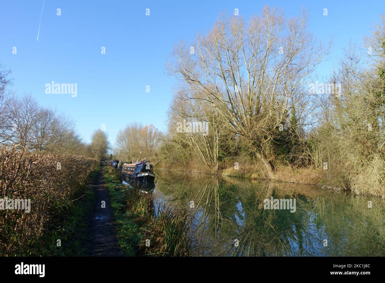 Barcos estrechos amarrados en el Canal Kennet & Avon, árboles bordeados de reflejos de espejo en un día de otoño con cielo azul, Hungerford, enero Foto de stock