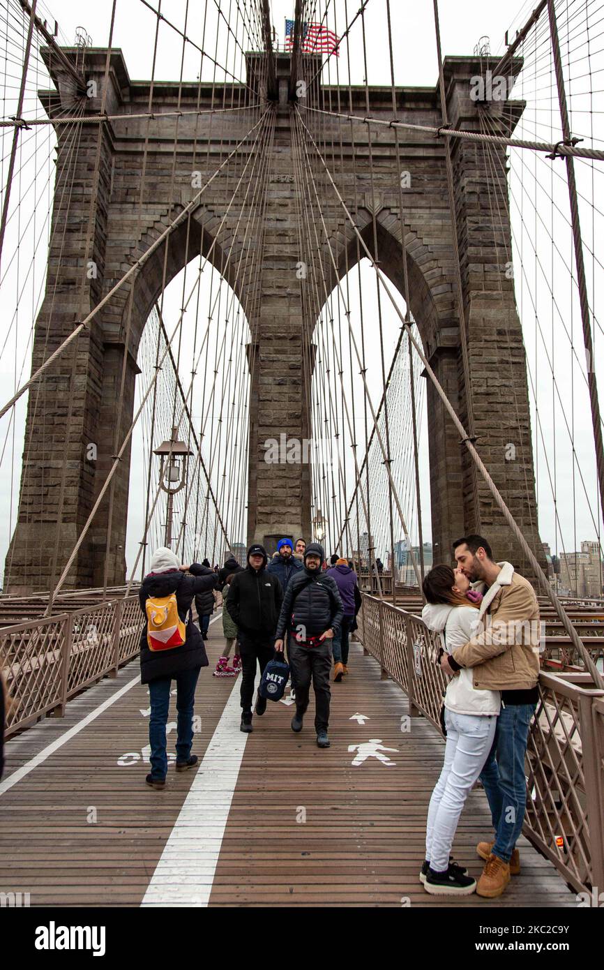 Una joven pareja besándose en el icónico puente de Brooklyn en la ciudad de Nueva York en los Estados Unidos, como se ve durante un día nublado con turistas y lugareños en él. El famoso puente, un punto de referencia para Nueva York y los Estados Unidos de América es un puente suspendido de cable híbrido que abarca el río East entre los distritos de Manhattan y Brooklyn. El histórico puente de Nueva York fue construido entre 1869 y 1883. Nueva York, EE.UU. El 13 de febrero de 2020 (Foto de Nicolas Economou/NurPhoto) Foto de stock