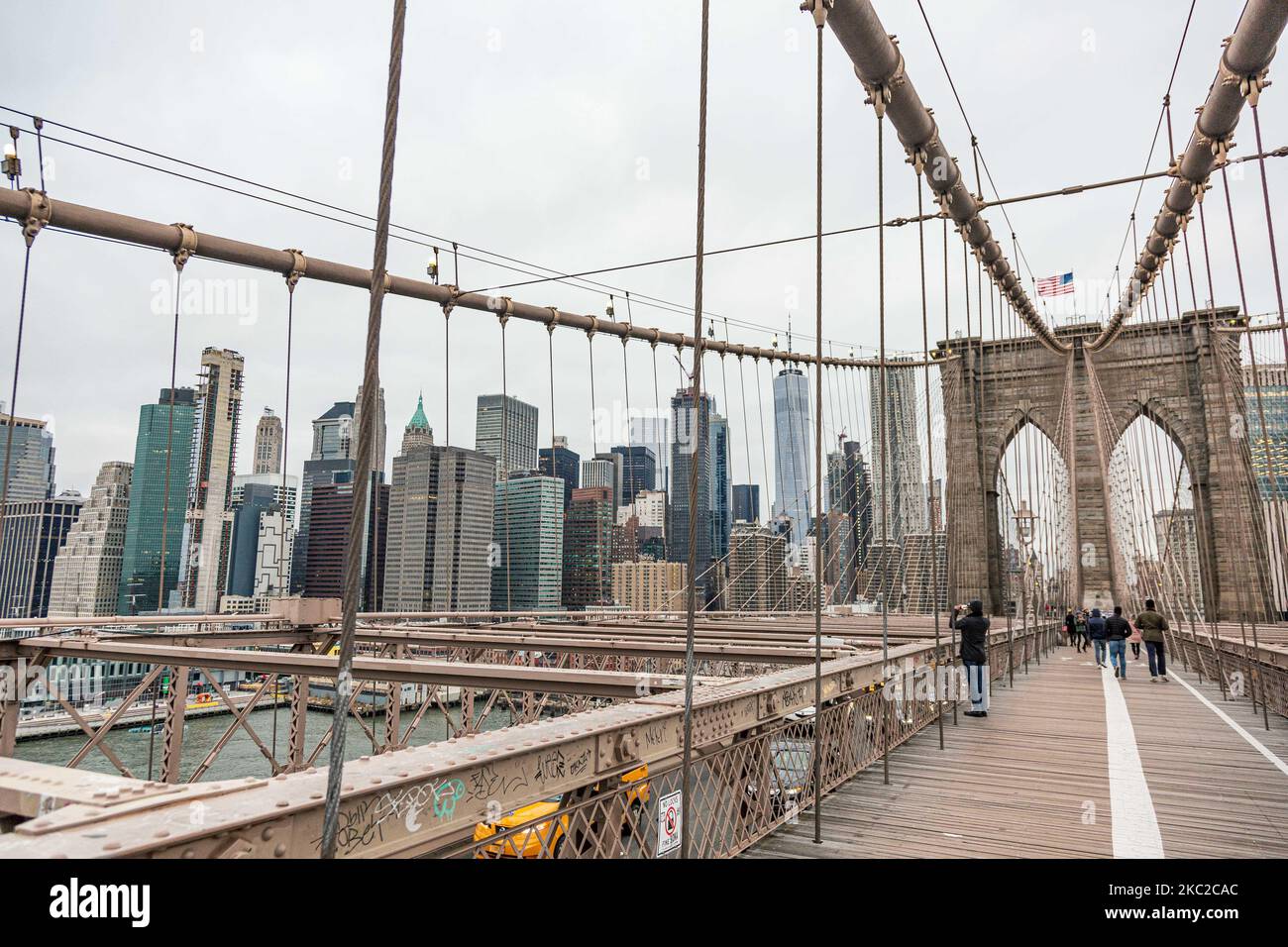 Vista desde el Puente de Brooklyn del centro de Manhattan. El puente de Brooklyn en la ciudad de Nueva York en los Estados Unidos, visto durante un día nublado con turistas y lugareños en él. El famoso puente, un punto de referencia para Nueva York y los Estados Unidos de América es un puente suspendido de cable híbrido que abarca el río East entre los distritos de Manhattan y Brooklyn. El histórico puente de Nueva York fue construido entre 1869 y 1883. Nueva York, EE.UU. El 13 de febrero de 2020 (Foto de Nicolas Economou/NurPhoto) Foto de stock