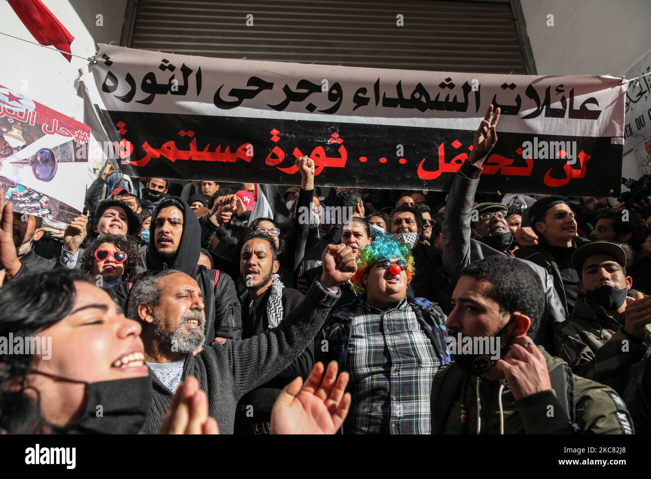 Los manifestantes cantan consignas antigubernamentales frente a un edificio del primer ministerio en Túnez, en el que las personas heridas durante la revolución tunecina celebraron una sentada para pedir la publicación de la lista final de mártires y heridos de la revolución en el Boletín Oficial de la República de Túnez (JORT). Una pancarta colocada en la entrada del edificio dice en árabe: «Familias de mártires y heridos de la revolución, no celebraremos, la revolución continúa». Túnez, 23 de enero de 2021. (Foto de Chedly Ben Ibrahim/NurPhoto) Foto de stock