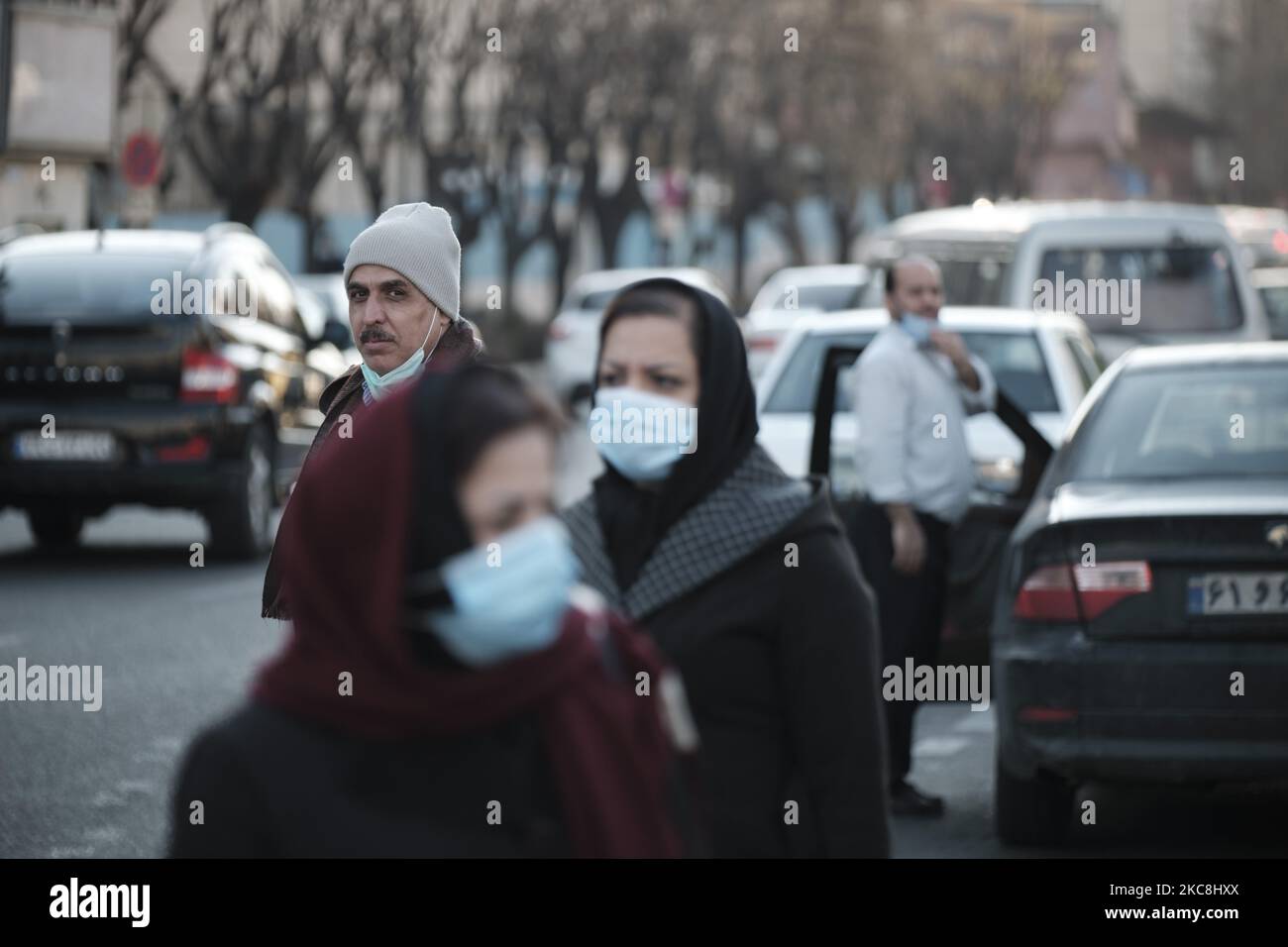 Un hombre iraní observa a dos mujeres con mascarillas protectoras mientras se encuentran de pie en una calle en la plaza Vanak, en el norte de Teherán, durante diez días de celebraciones del cuadragésimo segundo aniversario de la victoria de la Revolución Islámica de Irán, el 1 de febrero de 2021. (Foto de Morteza Nikoubazl/NurPhoto) Foto de stock