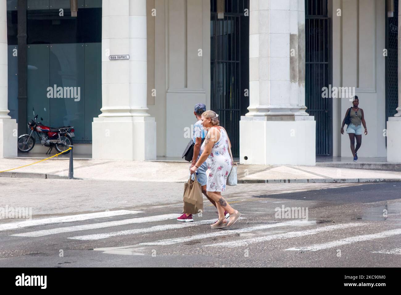 Una mujer mayor y un hombre cruzan la calle de la ciudad por una fuga de agua en el distrito del centro de la ciudad. Foto de stock