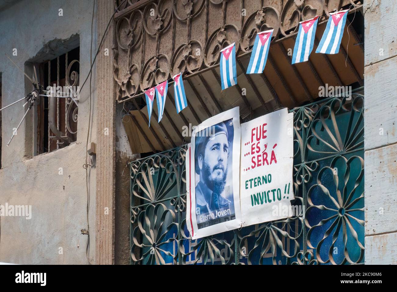 Una foto de Fidel Castro y pequeñas banderas cubanas están en un edificio envejecido. Un texto dice: 'Era, es, y será eterno, Invictus.' Foto de stock