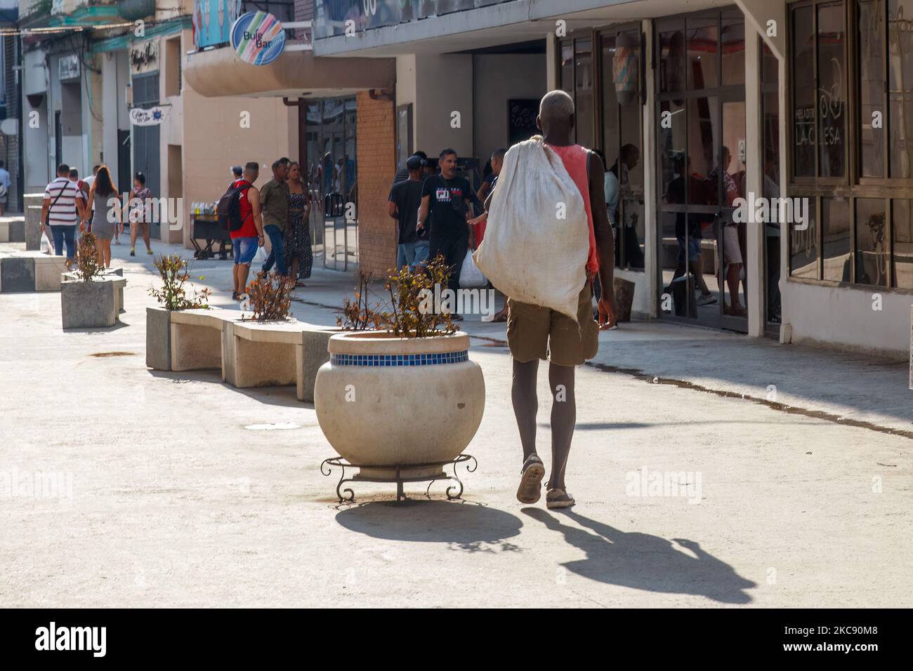 Un pobre y sucio hombre cubano en pantalones cortos lleva un saco mientras camina por un bulevar de la ciudad o una pasarela. Foto de stock
