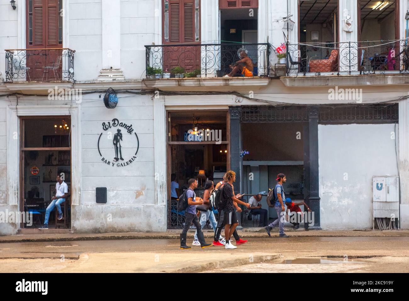 Un grupo de cubanos camina frente a una fachada de negocios. La casa está en la parte superior del segundo piso del edificio Foto de stock