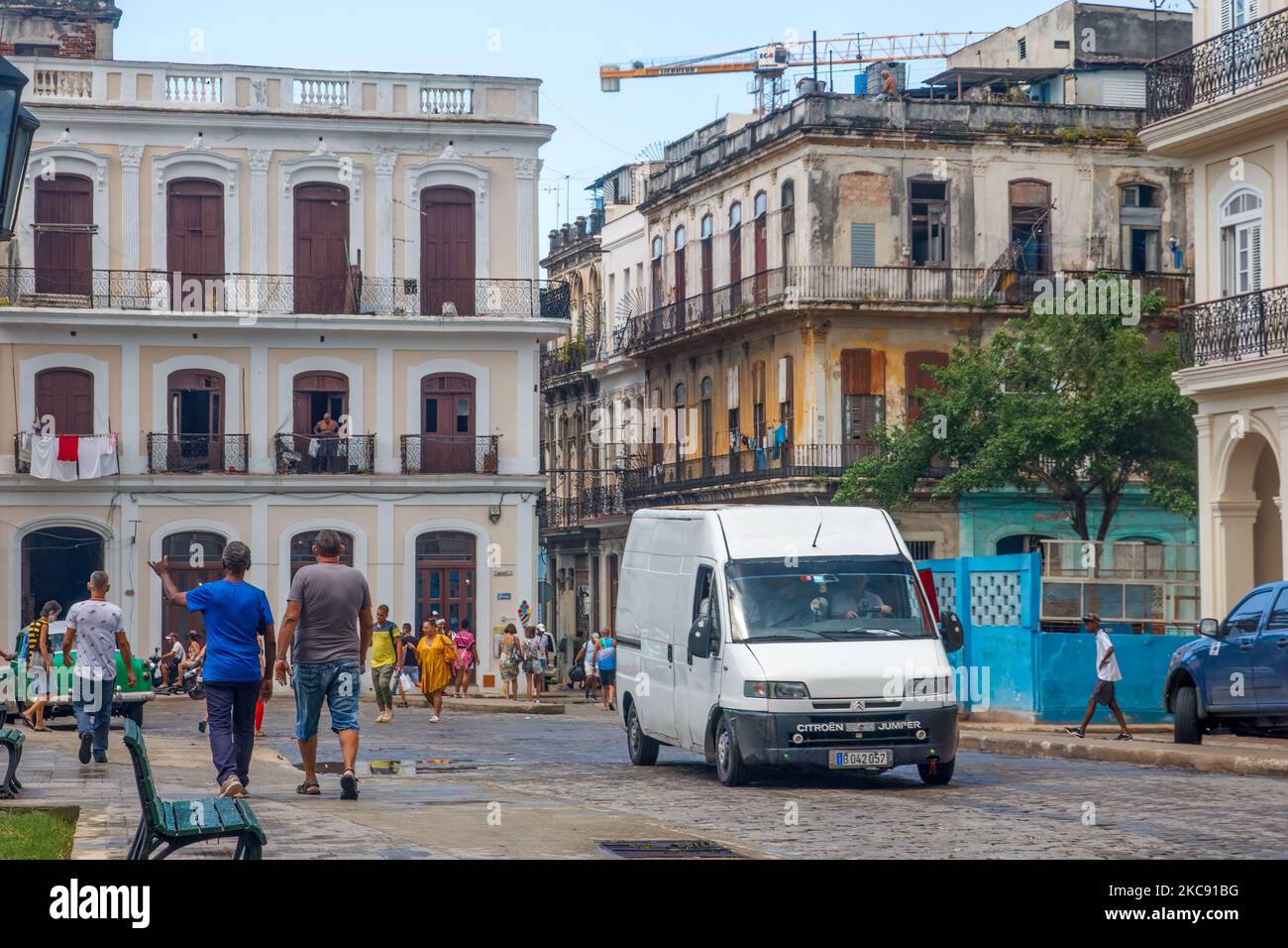 Un vehículo y el pueblo cubano están en una calle de la ciudad donde la arquitectura desgastada es común Foto de stock