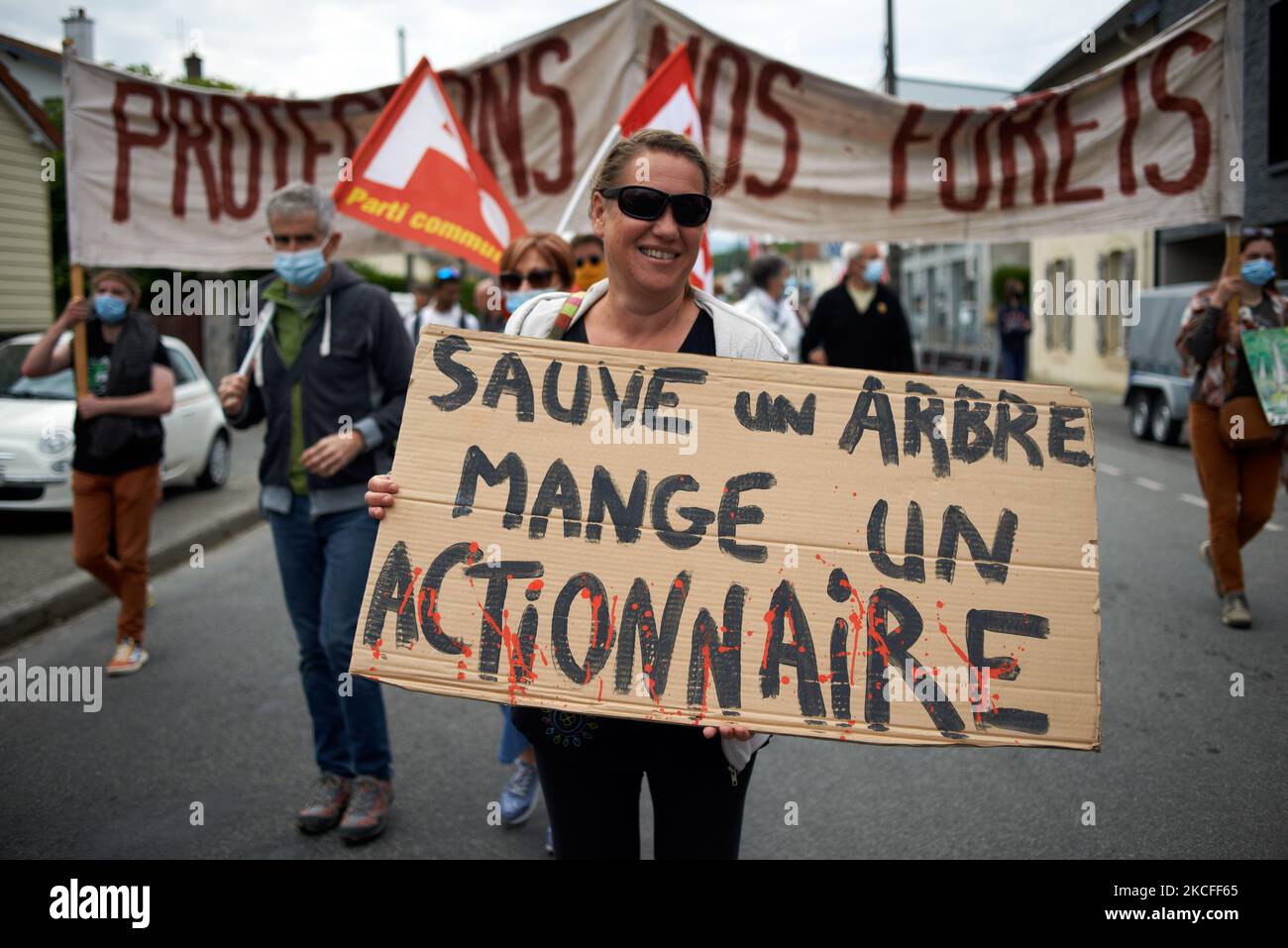 Una mujer sostiene un cartel que dice 'Salvar un árbol, comer un accionista'. Varias asociaciones, partidos políticos y personas unidas en un colectivo 'Touche pas a ma foret' (es decir, 'No toquen mi bosque') se manifestaron en Lannemezan (Altos Pirineos) como querían mostrar su oposición a una empresa global, Florian. Marcharon desde la estación de tren de Lannemezan hasta el ayuntamiento antes de establecer un campamento en Nestie. La empresa de aserradero Florian quiere construir un aserradero gigante cerca de la ciudad pirenaica de Lannemezan. Se espera que el aserradero trate casi 400,000 metros cúbicos de madera de haya cada año. Para esto Foto de stock