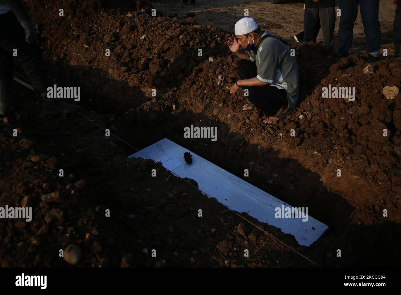 Usando ropa de protección (Hazmat) que dice ''Stop, Don't Add More'', (Stop Jangan Nambah Lagi) los funcionarios funerarios enterrarán los cuerpos de COVID-19 en el Cementerio Público de Rootan, North Jakarta, en 26,2021. Los oficiales de entierro han estado llevando a cabo sus tareas sin detenerse ya que hubo un aumento en el caso del virus Covid-19, enterraron los cuerpos de alrededor de 80 a 100 ataúdes Covid-19 más en un día de la mañana a la noche. (Foto de Dasril Roszandi/NurPhoto) Foto de stock