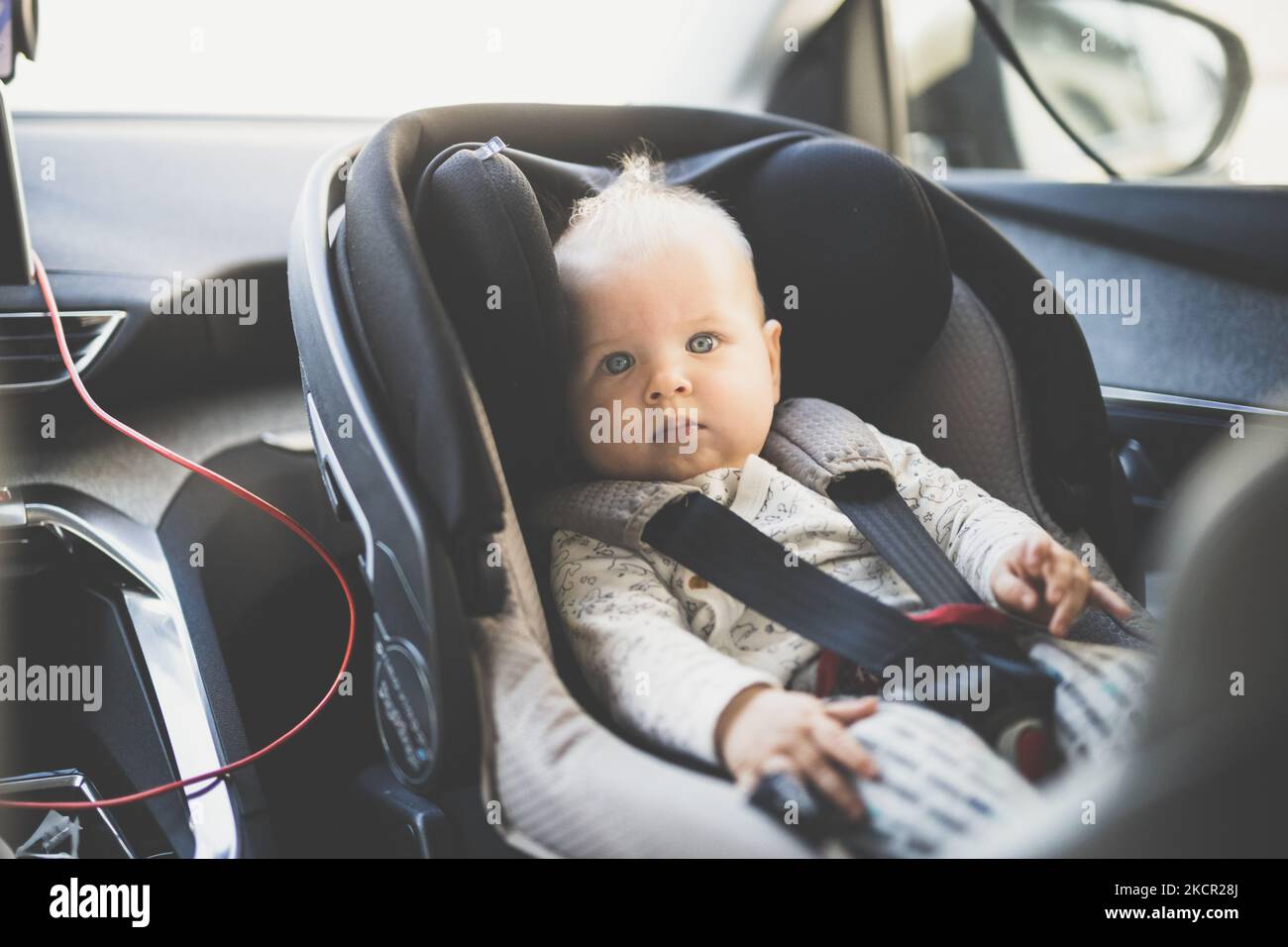 Lindo bebé niño atado con correa en el asiento de seguridad para niños en el compartimiento de pasajeros durante la conducción del automóvil Foto de stock