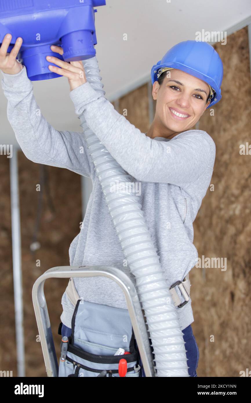mujer constructora instalando extractor de aire en el techo Foto de stock