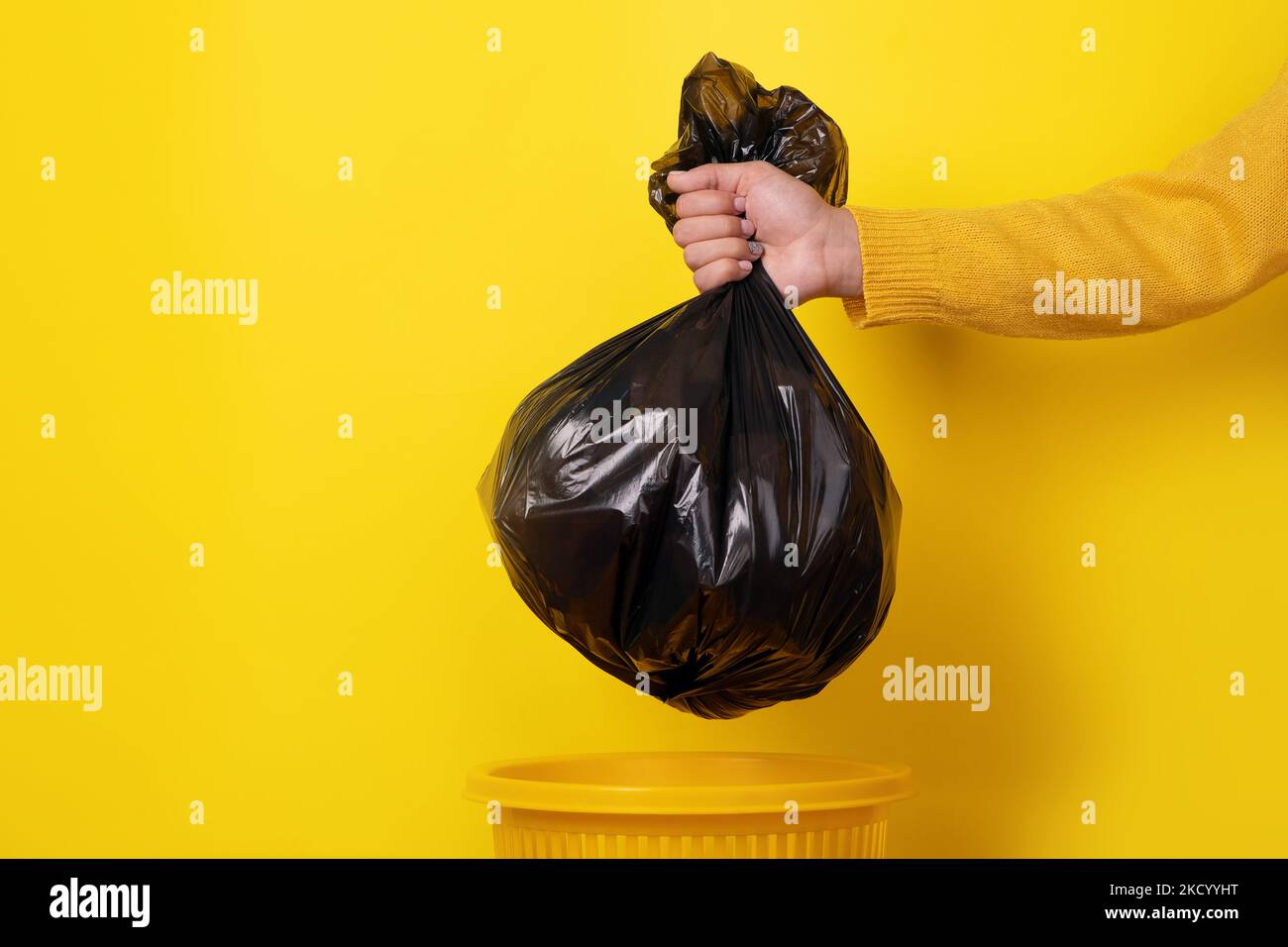 mano sosteniendo la bolsa de basura sobre fondo amarillo Foto de stock