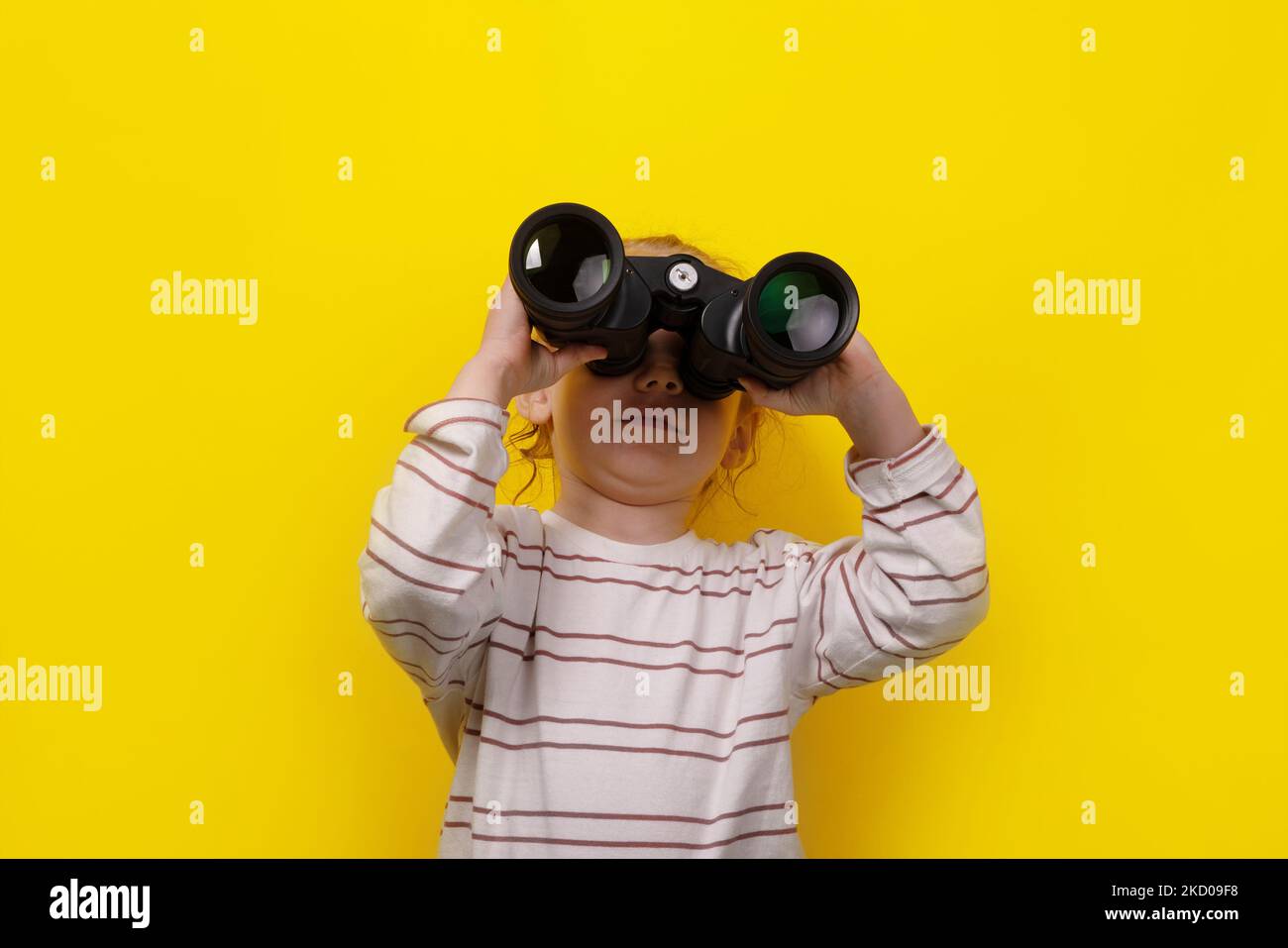 niña mirando a través de binoculares sobre fondo amarillo Foto de stock