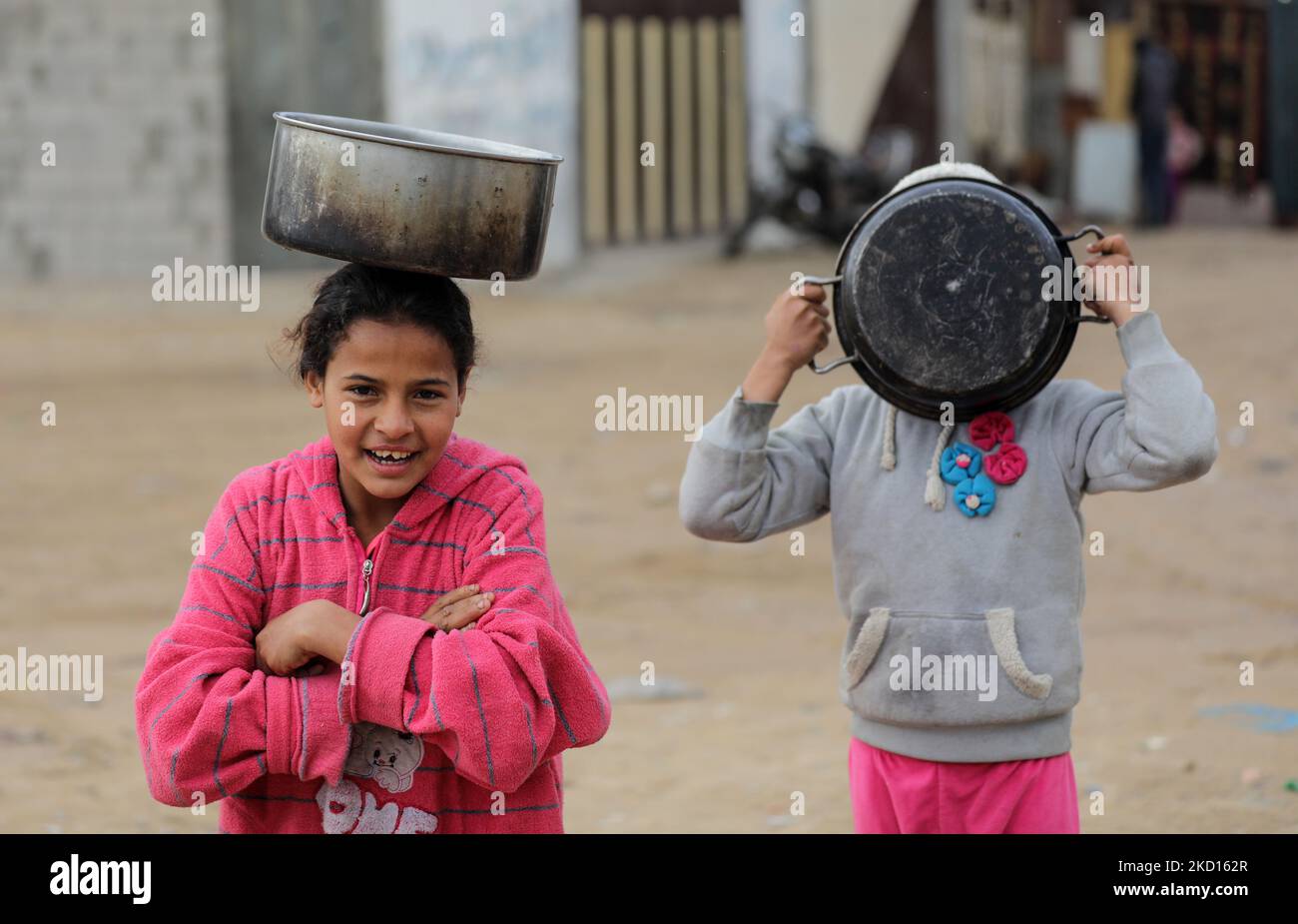 Los niños palestinos esperan con sus ollas para recibir comida gratuita cocinada por Amel Abu Amra (invisible) en un barrio pobre al este de la ciudad de Gaza, el 24 de enero de 2022. Amel Abu Amra, de 41 años de edad, pertenece a una familia pobre y recibe donaciones para cocinar alimentos destinados a alimentar a personas pobres como ella. (Foto de Majdi Fathi/NurPhoto) Foto de stock