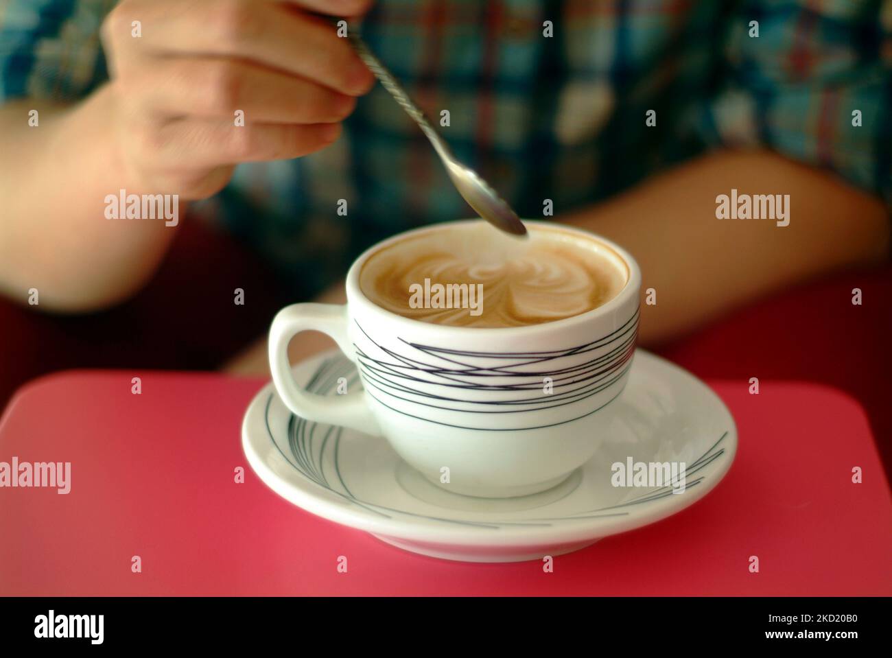 Un primer plano del cappuccino de bonito diseño en una taza blanca con una persona sujetando una cuchara por encima Foto de stock
