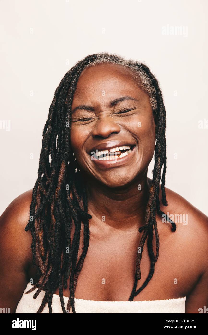 Mujer feliz sonriendo alegremente con una cápsula de ácidos grasos Omega 3 entre sus dientes. Mujer madura con dreadlocks usando suplementos nutricionales como Foto de stock