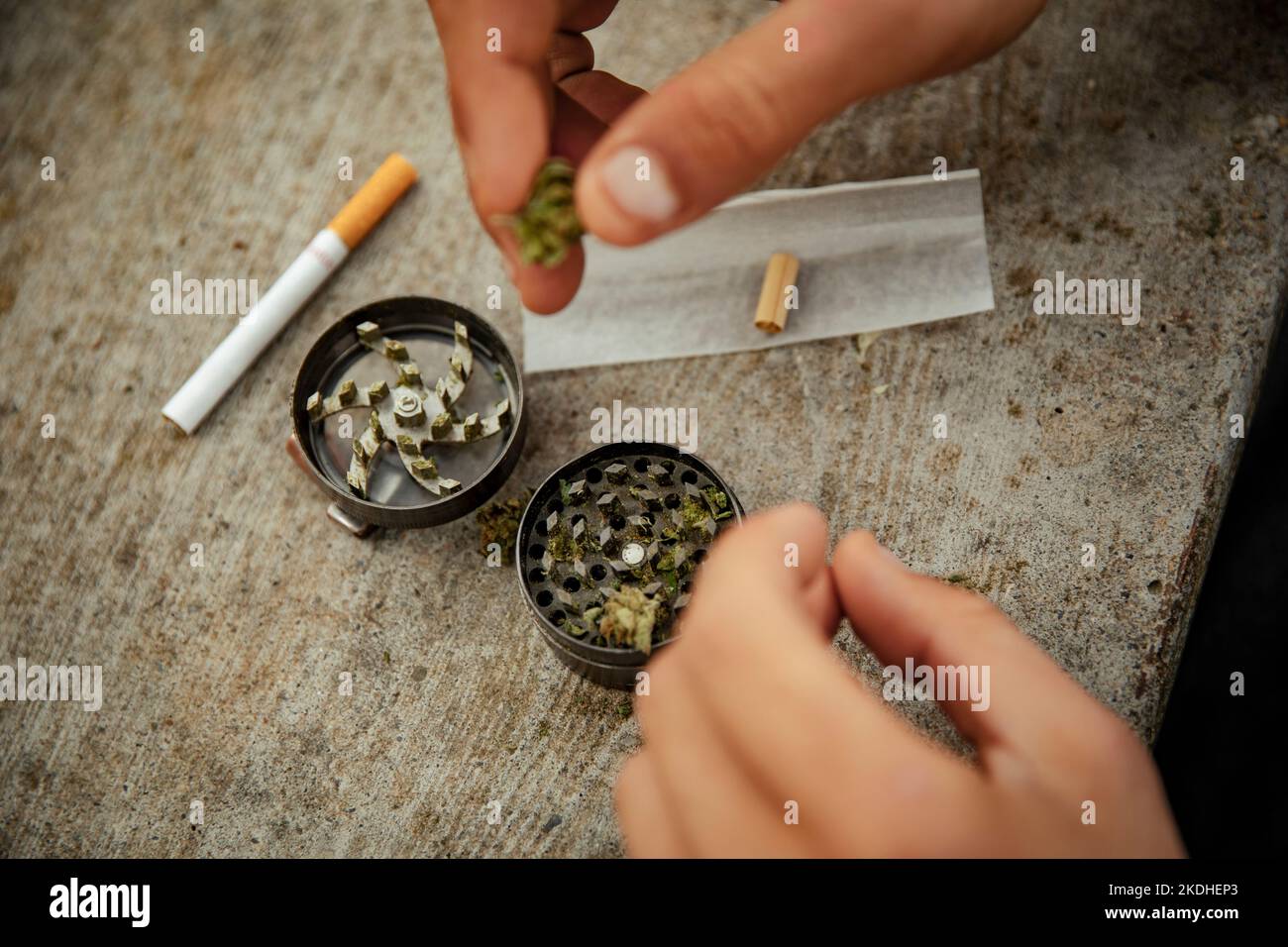 Manos de un niño preparando una articulación de marihuana con un molinillo Foto de stock