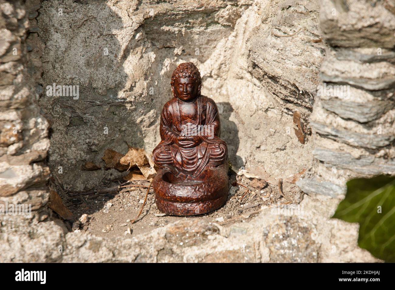 Una pequeña estatua del Buda en arcilla de Yixing se encuentra en una pared de piedra para objetos religiosos en un patio trasero de Filadelfia. Foto de stock