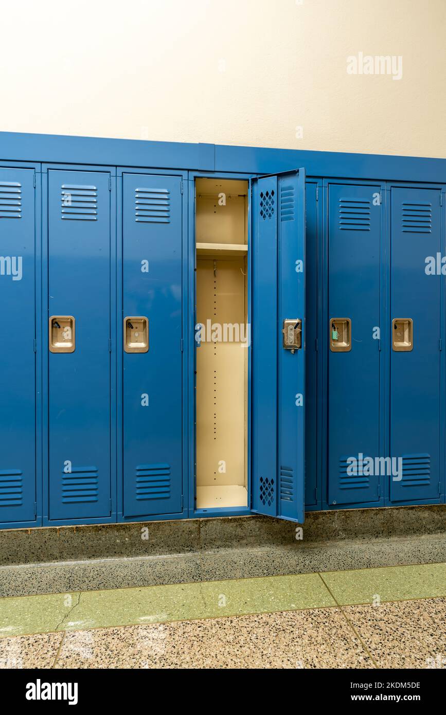 Casillero de metal azul vacío y abierto a lo largo de un pasillo indescriptible en una típica escuela secundaria de los Estados Unidos. No se incluye información identificable en la sala. Foto de stock