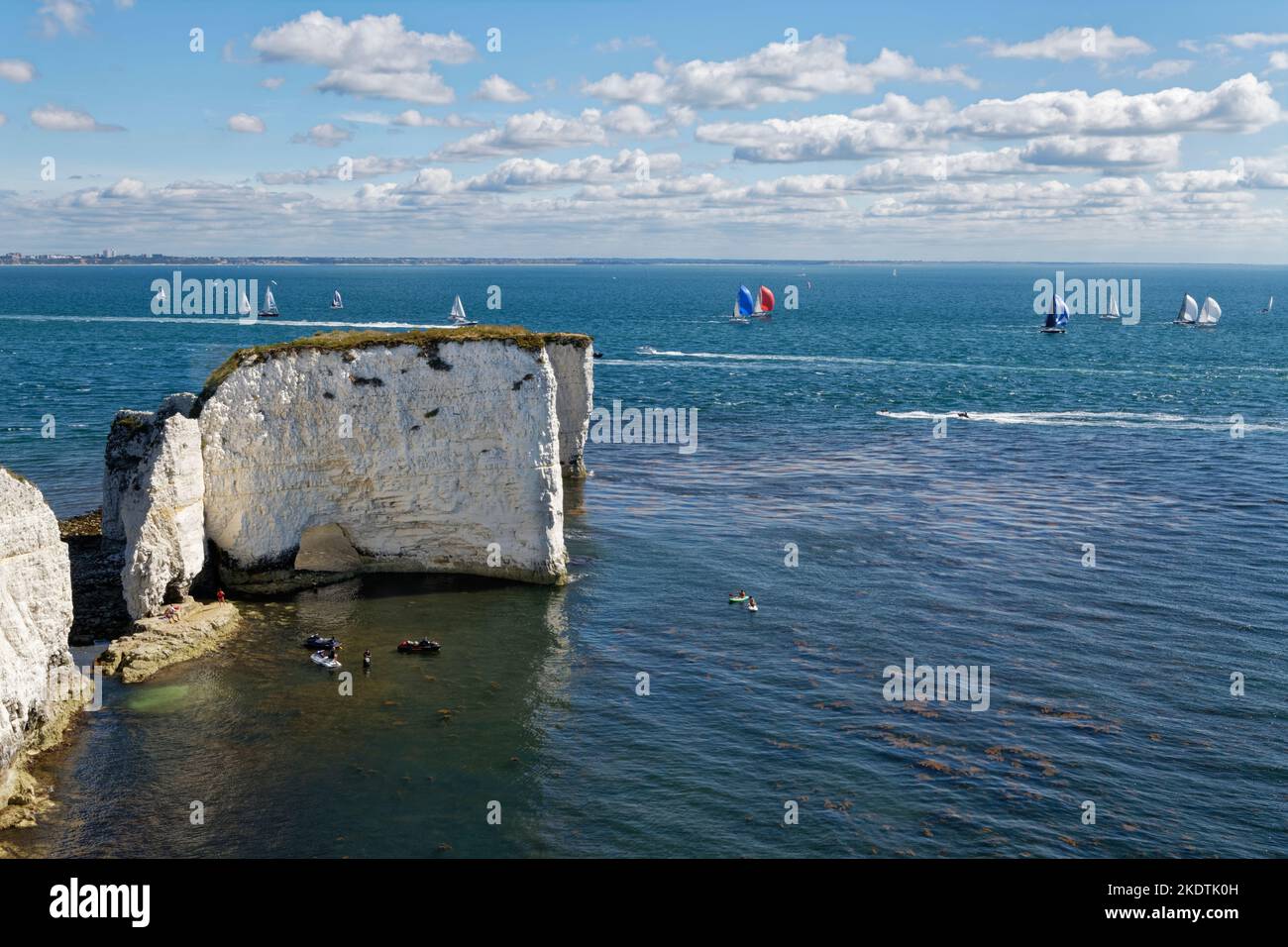 Old Harry’s Rocks con gente en motos de agua y tablas de paddle cerca y una regata de vela en el fondo, Studland, Dorset, Reino Unido, julio. Foto de stock