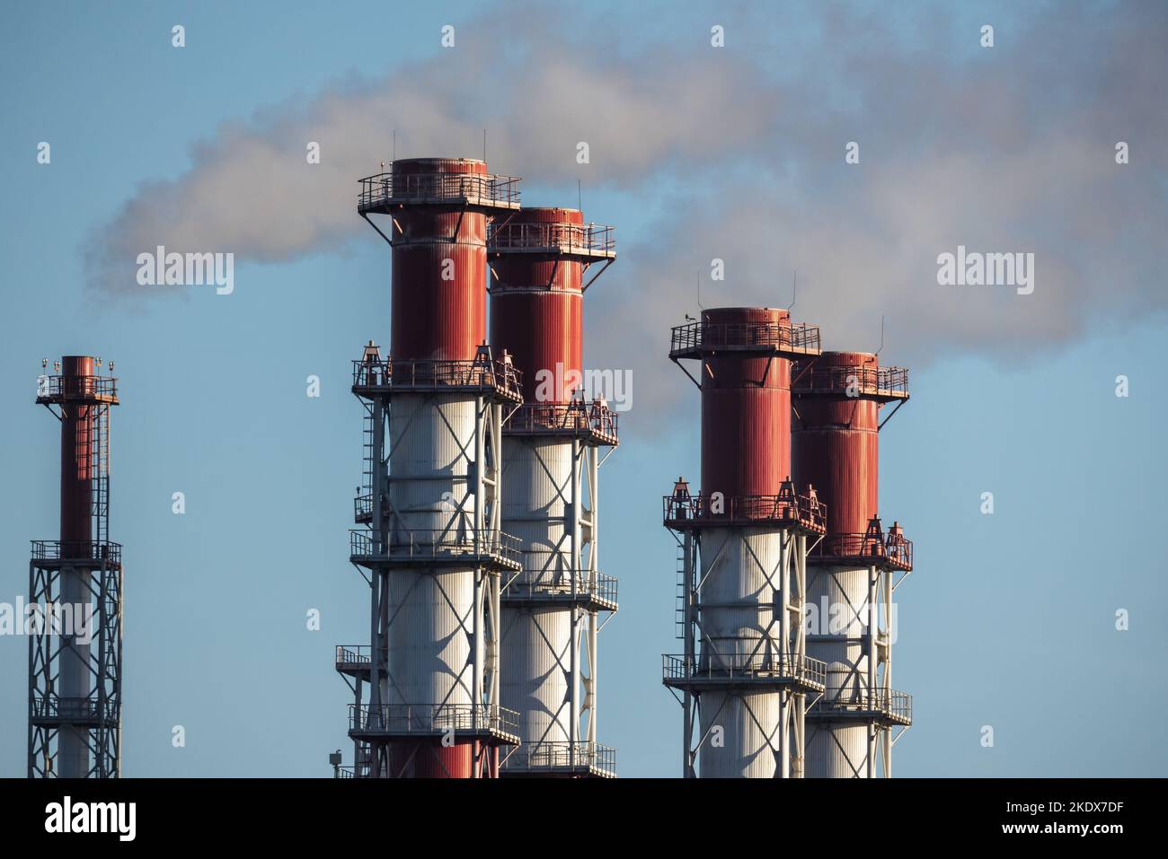 Las chimeneas de metal blanco y rojo están bajo el cielo azul durante el día. Equipo de la central eléctrica Foto de stock