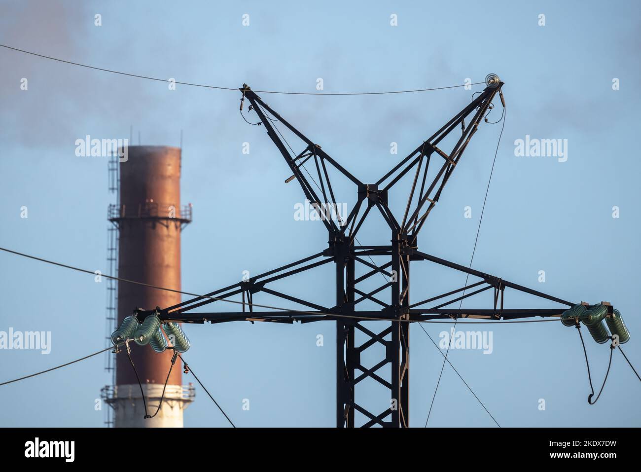 La torre de la línea de energía aérea de acero tipo celosía y la chimenea de la planta de energía eléctrica están bajo el cielo azul Foto de stock