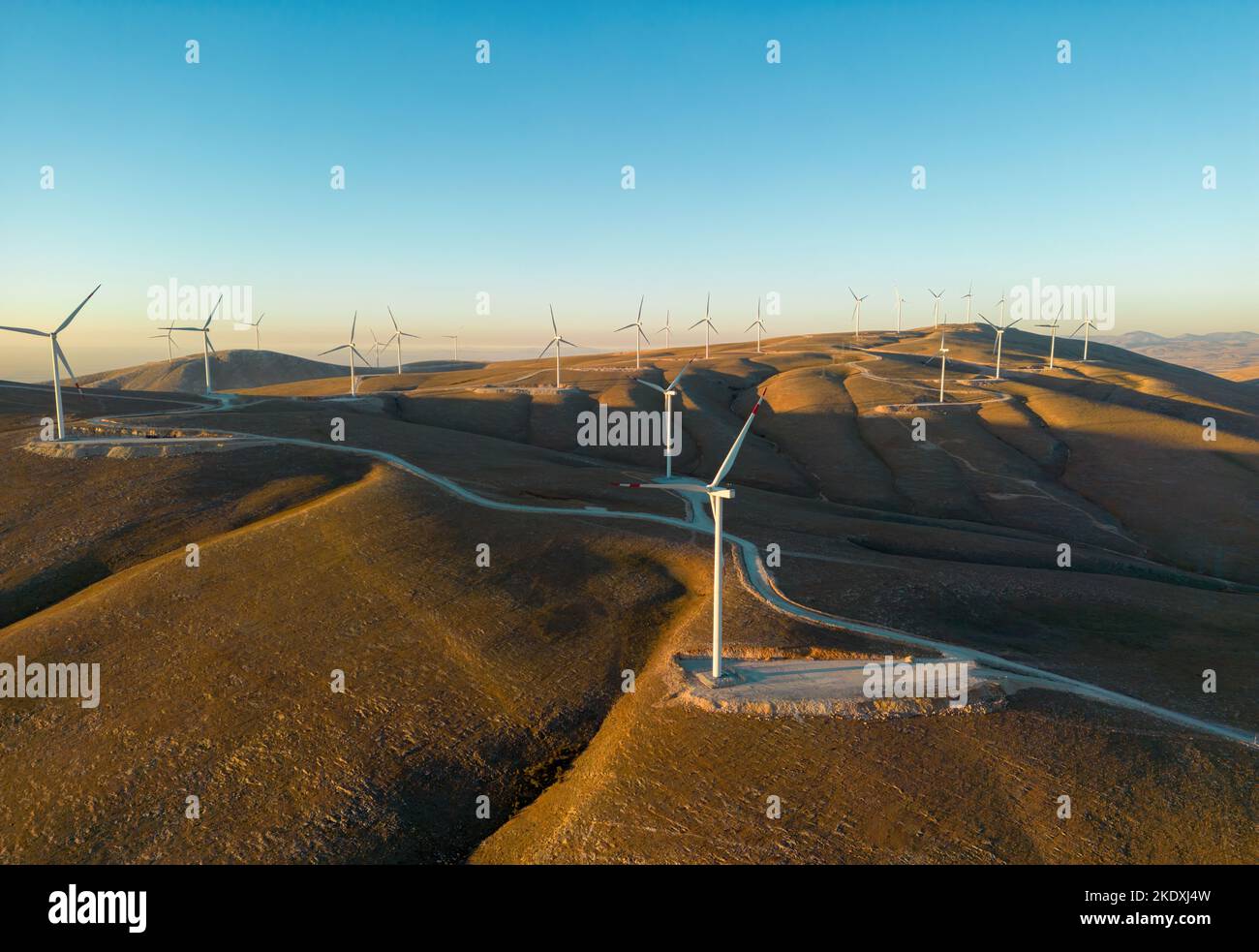 Vista aérea de múltiples aerogeneradores parados en una colina y generando electricidad al amanecer Foto de stock