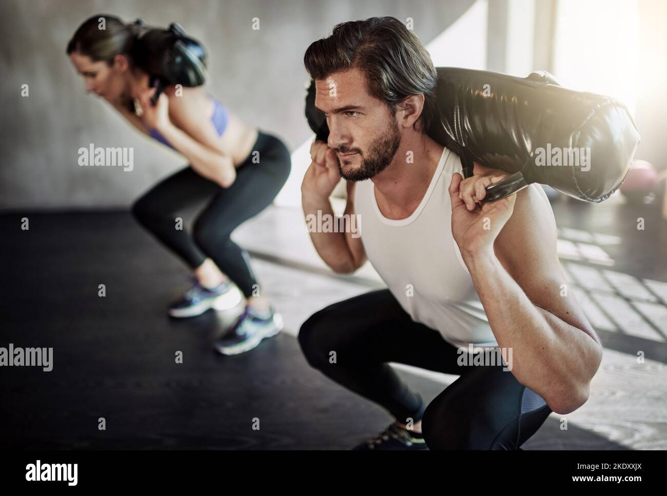 Renunciar no es una opción, dos jóvenes haciendo ejercicio en el gimnasio usando bolsas de peso. Foto de stock