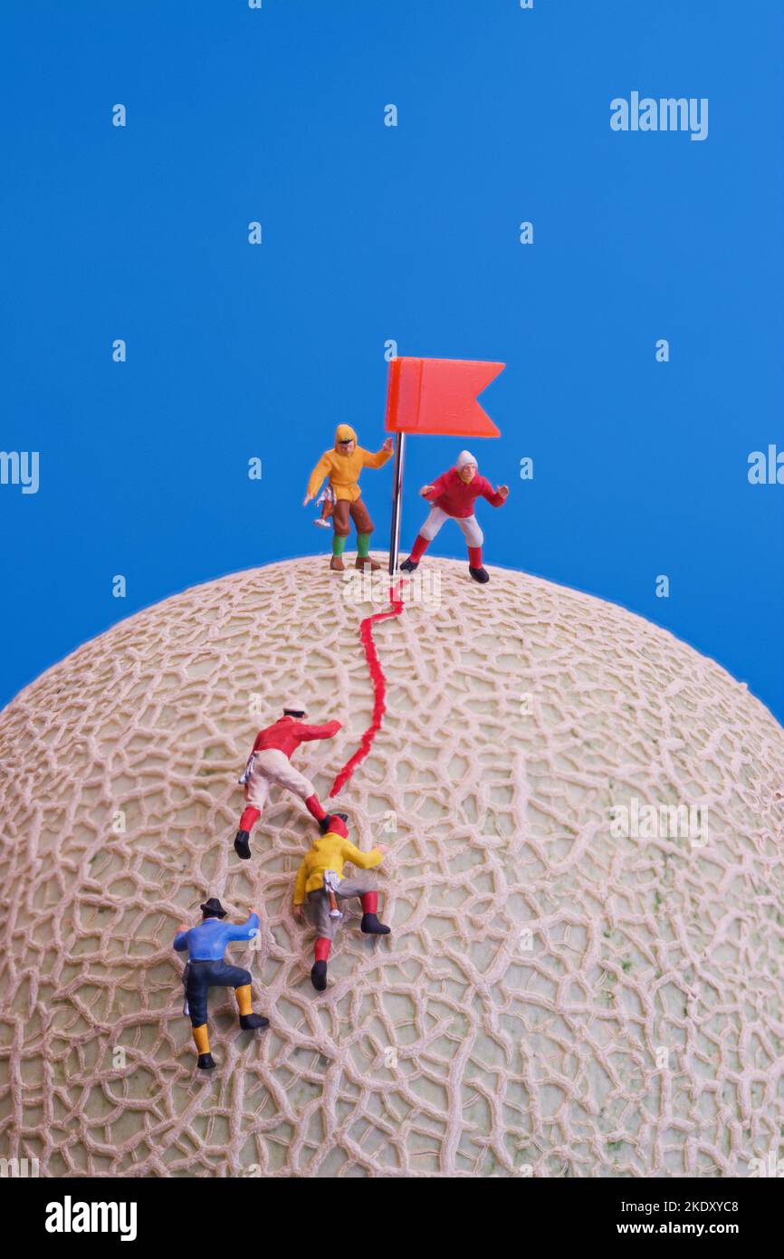 Juguetes en miniatura - Un grupo de escaladores de montaña que llegan a la cima. La fruta del melón de la roca como la base. Foto de stock